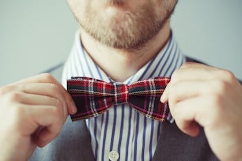 Close-up photo of a man with bard correcting his bow-tie