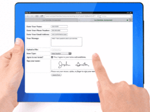 A tablet computer with a fillable form on it. One hand holds the tablet, the other one signs the form with an index finger.