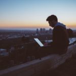 Man sitting on ledge with computer overlooking a city