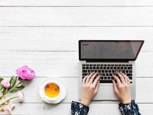 Hands typing on a laptop with flowers and a cup of tea nearby