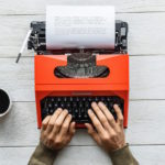 Hands typing on an orange typewrite