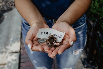 Someone's hands holding coins and a sheet of paper saying, "Make a change"