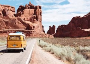 Vanagon driving down road towards desert rocks