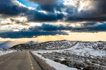 A hilly, rural road with storm clouds and snow on the ground